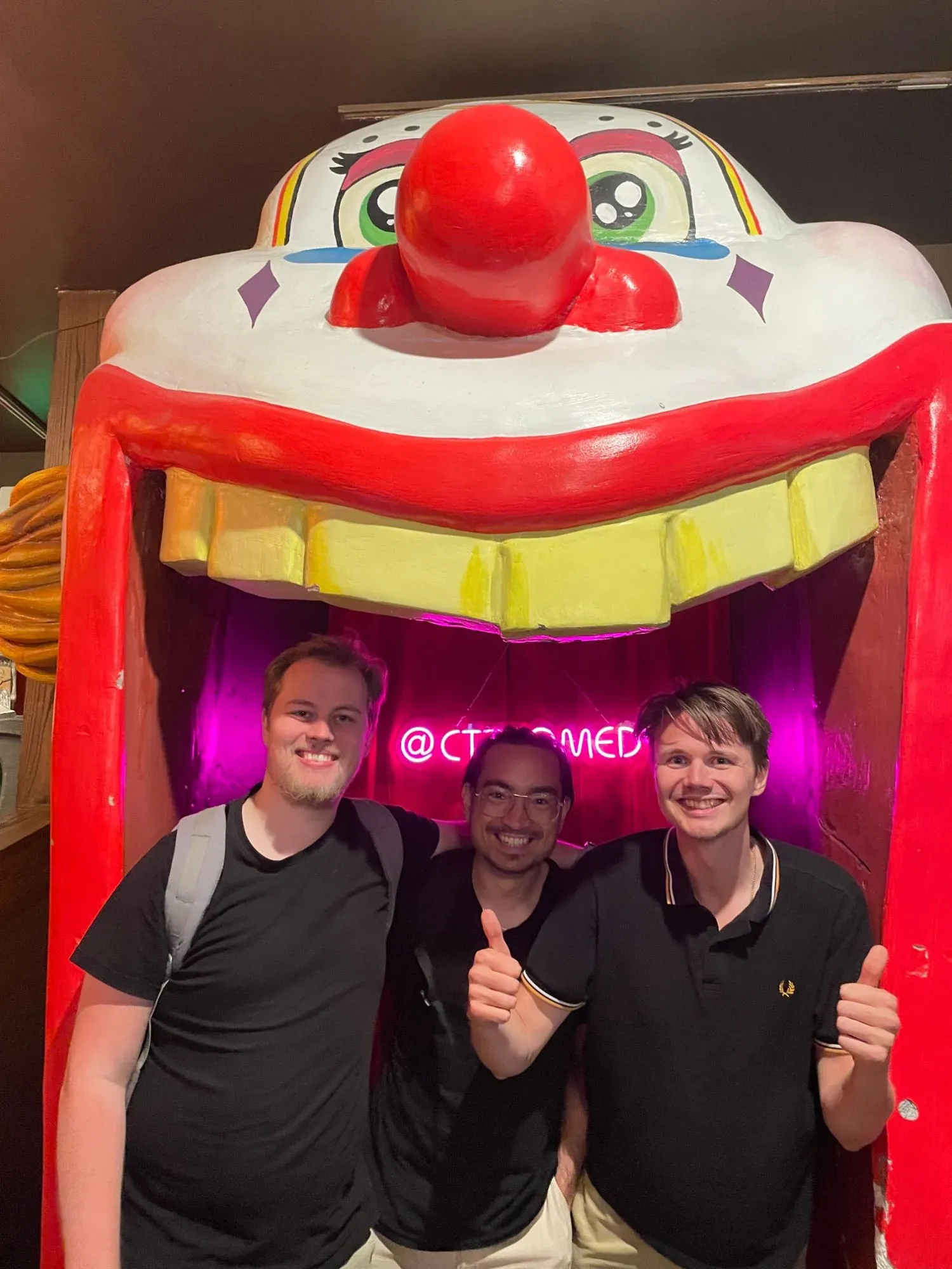 David giving a thumbs up with two of the team inside a giant clown mouth at a comedy club