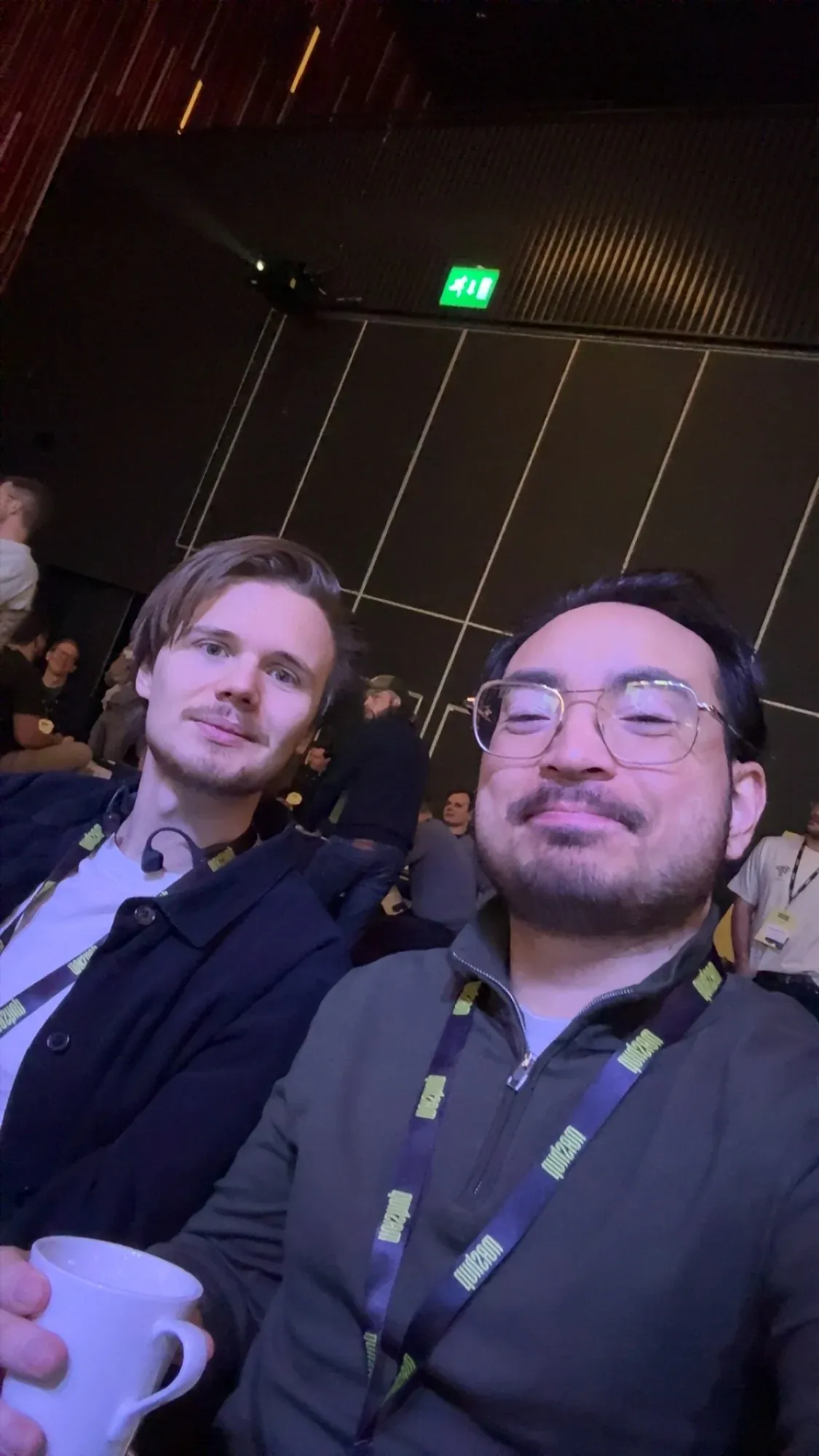 A selfie of David and Fredric with lanyards in a dark auditorium