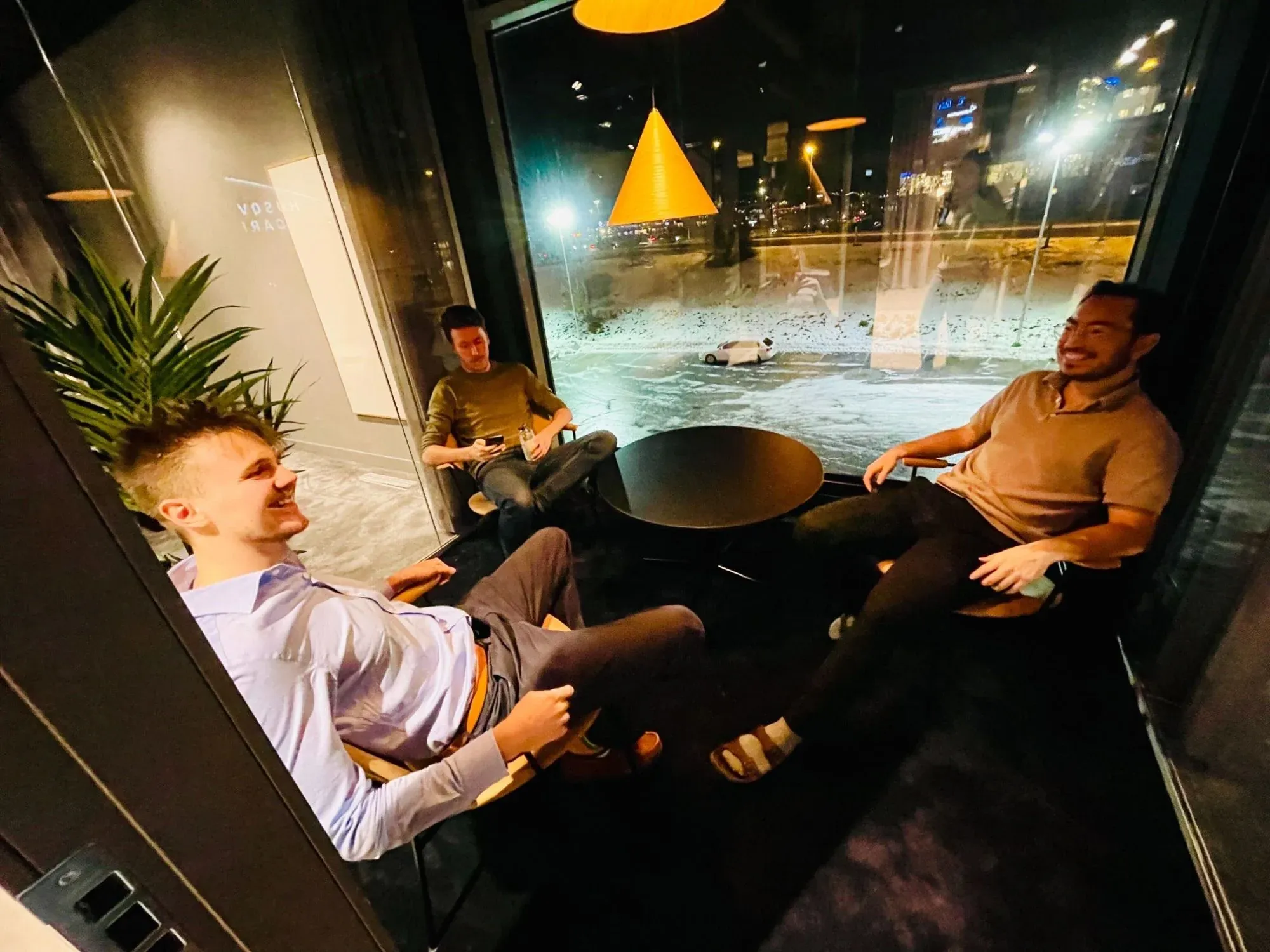 Three of the team laughing in a glass meeting room at night, snow outside