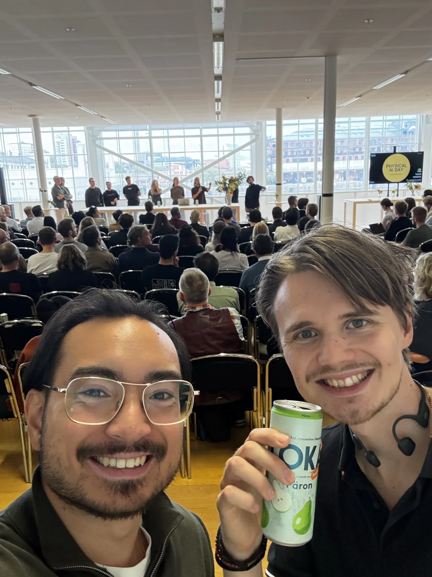 A selfie of Fredric and David in the audience, Physical AI Day on the screen behind them