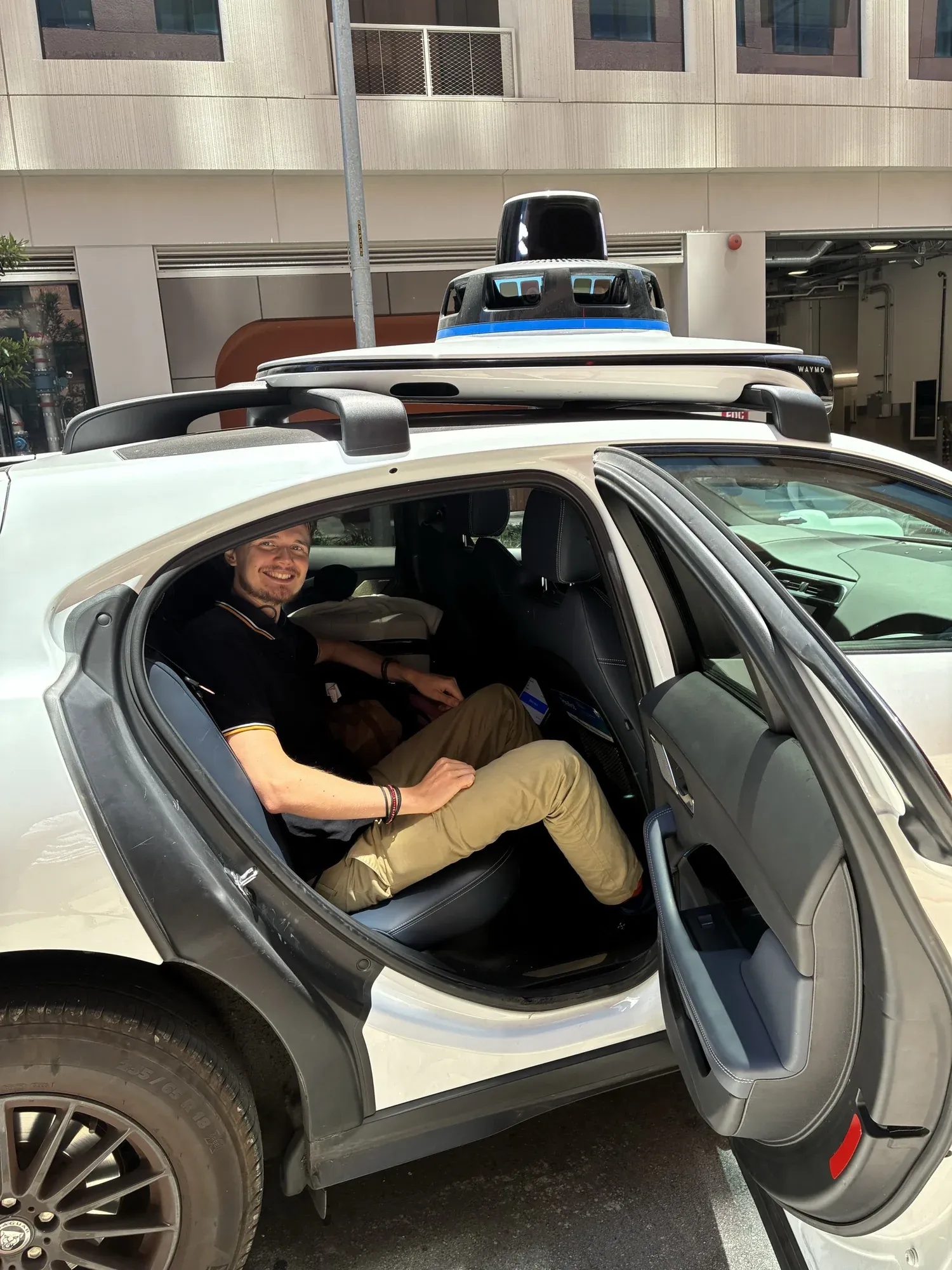 David smiling from the back seat of a Waymo with no driver, its sensors on the roof