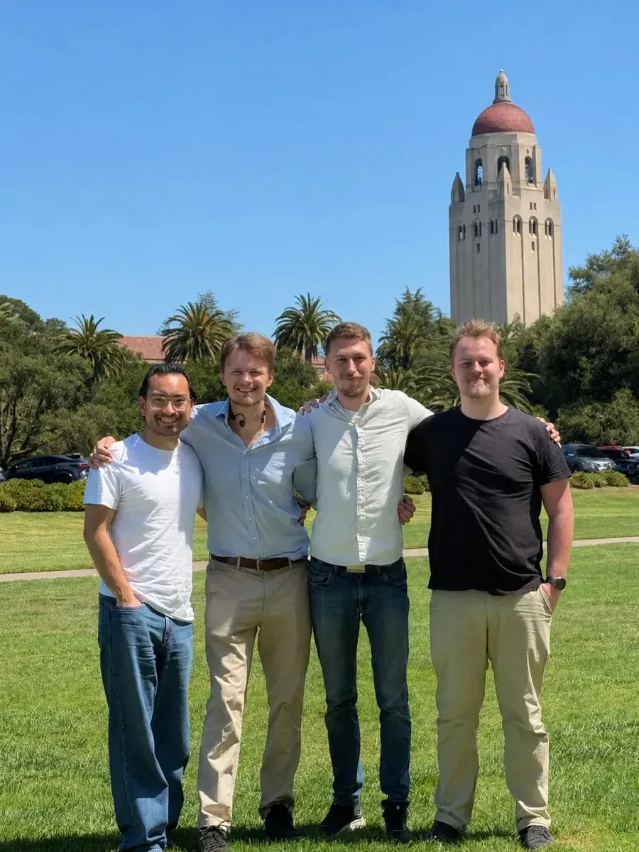 Four of the team arm in arm on the lawn at Stanford, Hoover Tower behind them